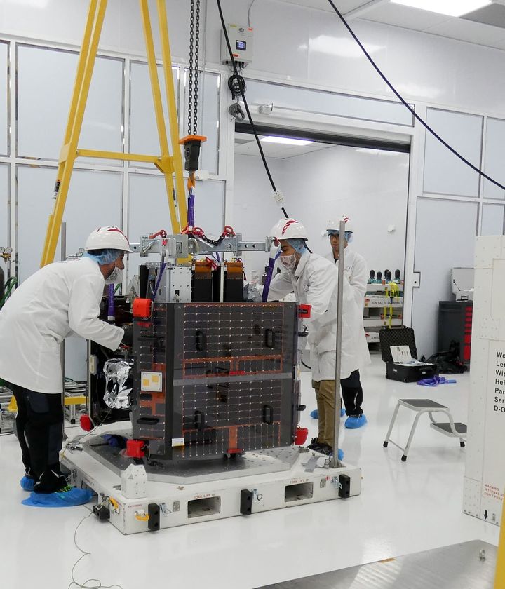 Engineers in white cleanroom suits lifting a satellite on a transport pallet